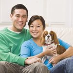 A young Asian couple sitting on a couch together and holding a dog.