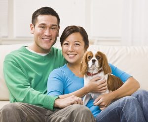 A young Asian couple sitting on a couch together and holding a dog.