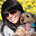 Woman wearing sunglasses holding a dog with his tongue sticking out.
