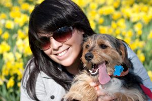 Woman wearing sunglasses holding a dog with his tongue sticking out.