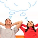 photo of man and woman sitting on couch with their hands behind their necks. A drawn "thinking cloud" is above their heads