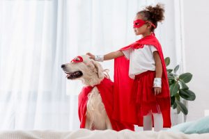 Young girl and dog both wearing red capes.