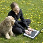 Young woman and dog sitting on the grass looking at a laptop computer