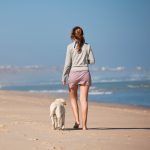 Young woman walking with her dog on the beach